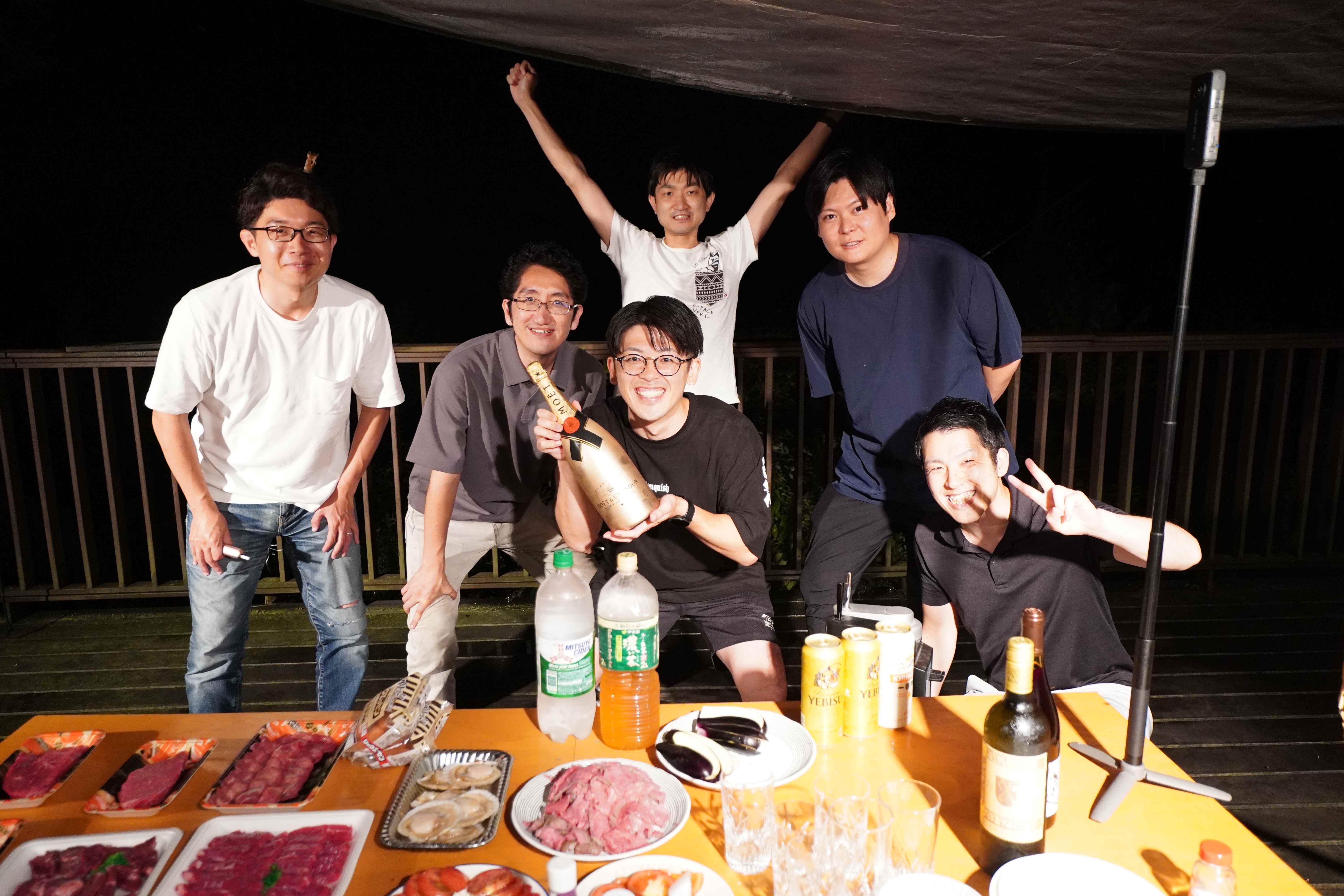 ロッジでバーベキューを楽しむメンバーの集合写真
